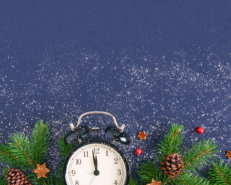 Christmas card. Brushing a branch of a tree on a dark blue background with red balls and figurines of shiny stars on white snow. Black retro alarm clock with stitches at 23.55 pm. Festive backgroundの写真素材