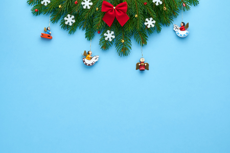 Christmas card. Branches of Xmas tree, folded in a triangle, decorated with a red bow, white snowflakes, bright stars, small bells, on a blue festive background. Background for your text and designの写真素材