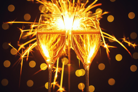 Holiday dynamic postcard. Two glasses with champagne wine and lighted fireworks on a glitter background with bright gold lights of a night city. Meeting the new year. Christmas party. Xmas holidayの写真素材