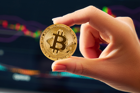 One golden bitcoin in a woman's hand on a bright background of business graphics close-up. Bitcoin-Crypto currency. Anonymousの写真素材