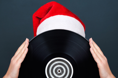 Christmas picture. A young woman in a red Santa Claus hat holds a black vinyl record for the turntableの写真素材