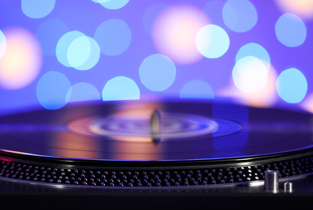 Blurred turntable vinyl record player. Sound technology for DJ to mix & play music. Vintage vinyl record player on a background decorations for a party, bright disco lightsの写真素材