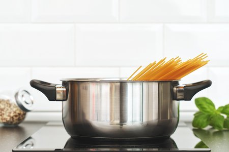 Home kitchen. Cooking food for lunch. Saucepan with spaghetti on the hob. Leaves of basil and seasoning. Background for your text and designの写真素材