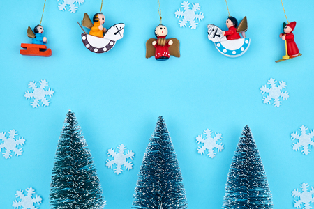 Christmas card decorated with three Christmas fir-trees, white snowflakes, wooden toys on a blue backgroundの写真素材