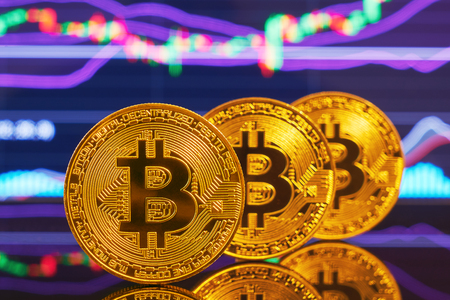 Three golden bitcoin are stacked on a bright background of business graphs close-up. Bitcoin cryptocurrency. Anonymousの写真素材