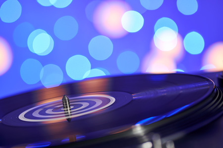 Blurred turntable vinyl record player. Sound technology for DJ to mix & play music. Vintage vinyl record player on a background decorations for a party, bright disco lightsの写真素材