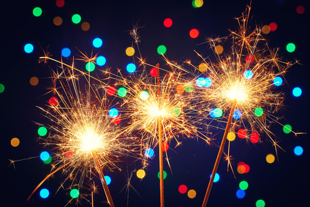 Holiday dynamic postcard. Three lighted fireworks on a blurred background of a bright Christmas garland. Meeting the new year. Christmas evening. Blur bottles on backgroundの写真素材