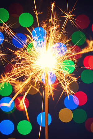 Holiday dynamic postcard. A lighted fireworks on a blurred background of a bright Christmas garland. Meeting the new year. Xmas  evening. Blur bottles on backgroundの写真素材