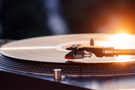 Turntable vinyl record player on the background of a sunset over the lights city. Sound technology for DJ to mix & play music. Black vinyl record. Vintage vinyl record player. Needle on a vinyl recordの写真素材