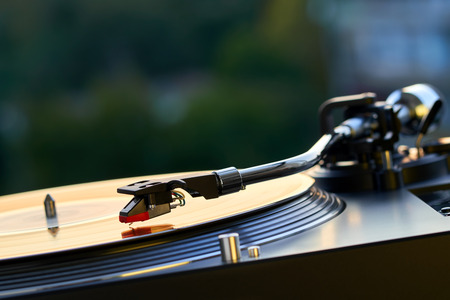 Turntable vinyl record player on the background of a sunset over the lights city. Sound technology for DJ to mix & play music. Black vinyl record. Vintage vinyl record player. Needle on a vinyl recordの写真素材