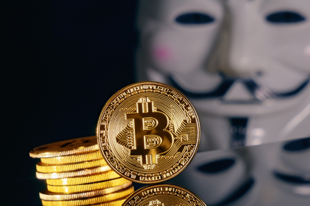 Crypto currency. Gold coins bitcoin on a dark background and a blurred golden mask Anonymousの写真素材