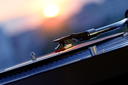 Turntable vinyl record player on the background of a sunset over the lights city. Sound technology for DJ to mix & play music. Black vinyl record. Vintage vinyl record player. Needle on a vinyl recordの写真素材