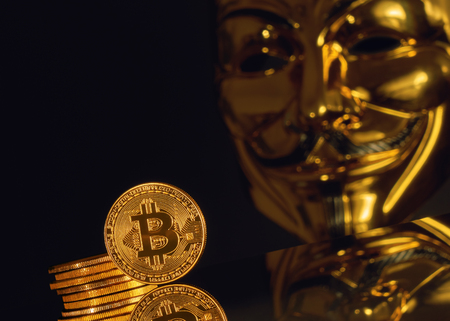 Crypto currency. Gold coins bitcoin on a dark background and a blurred golden mask Anonymousの写真素材