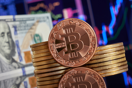 Golden bitcoin  stacked on a bright background of business graphs close-up. Litecoin cryptocurrency. Folded in a tube 100 dollar bills. Anonymous. Virtual currencyの写真素材