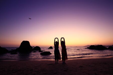 Two women by the sea, silhouetted by the setting sunの写真素材