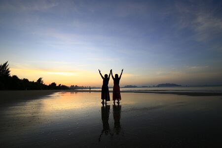 Two women by the sea, silhouetted by the sunriseの写真素材