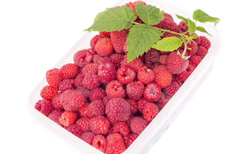 Sweet tasty ripe raspberries with green leaf in plastic box, isolated on white background
