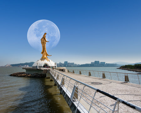Macau - October 29, 2014 : statue of kun lam, religion sacred landmark and buddhists tourism. Famous tourist attractions. Astronomical phenomenon, Full moon during day Behind the Goddess of Mercy.の写真素材