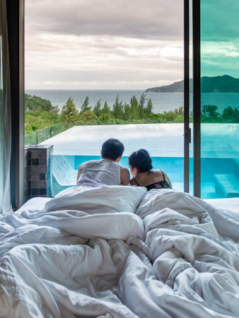 Back view of couple lying on bed under white blanket. Morning in bedroom by the window overlook...