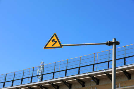 The sign of curve beside the railway bridge is in the background of blue skyの写真素材
