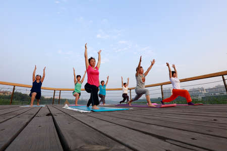LUANNAN COUNTY, China - July 28, 2018: People practice outdoor yoga on wooden platforms in the park, LUANNAN COUNTY, Hebei Province, Chinaのeditorial素材