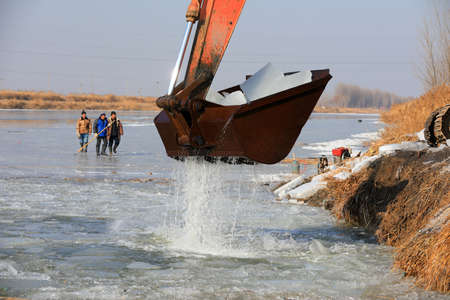 LUANNAN COUNTY, Hebei Province, China - January 14, 2020: Farmers use excavators to load ice in a...