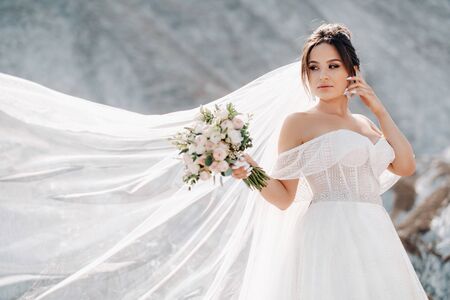 Beautiful bride in a wedding dress with a bouquet on the top of the salt mountains. A stunning young bride with curly hair . Wedding day. . Beautiful portrait of the bride without the groom.の写真素材