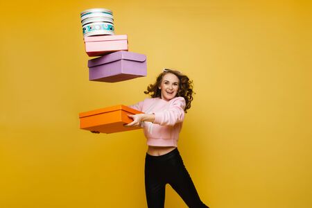 A happy young woman with colorful paper boxes after shopping isolated on an orange Studio background. Seasonal sales, purchases, spending money on gifts.の写真素材
