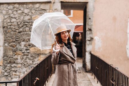 beautiful romantic girl in a coat and hat with a transparent umbrella in Annecy. France. The girl in the hat in France.の写真素材