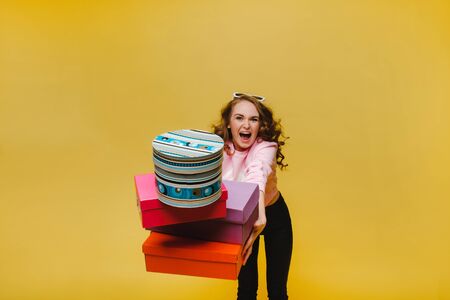 A happy young woman with colorful paper boxes after shopping isolated on an orange Studio...