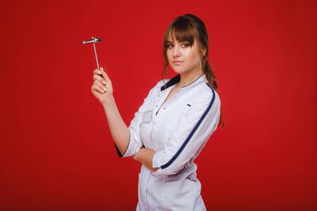 a beautiful doctor girl holds a reflex hammer and smiles at the camera isolated on a Red background.の写真素材