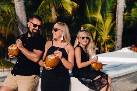 a stylish family in black clothes with coconuts in their hands on the beach of the island of...