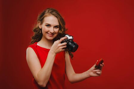 a smiling young woman with wavy hair holds a strawberry and photographs it, holding a delicious fresh strawberry on a bright red background.の写真素材