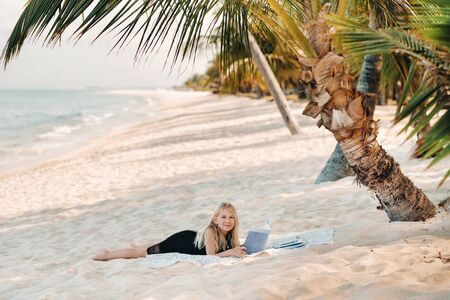 a little girl lies and enjoys the tropical beach of Le Morne in Mauritius.A girl reads a book on a beach in Mauritiusの写真素材