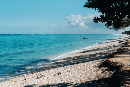 View of the white beach and turquoise ocean with a moored motor boat off the coast of Mauritius.の写真素材