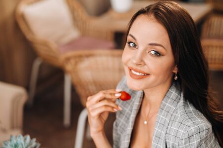 a woman is sitting in a cafe and eating strawberries.A girl with strawberries in her hands in a coffee shopの写真素材