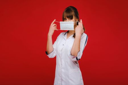 A female doctor stands in a medical mask isolated on a red backgroundの写真素材