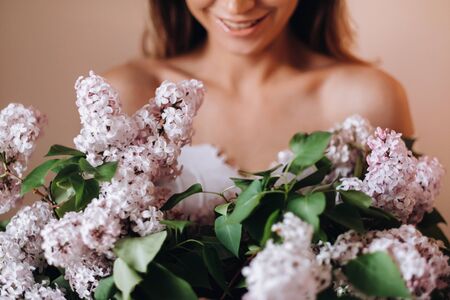 Beautiful girl with lilac flowers in her hands. A girl with lilac flowers in the spring at home. A girl with long hair and lilac in her hands.の写真素材