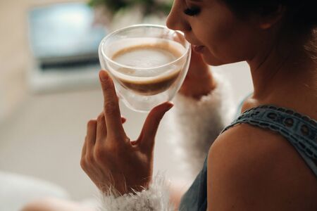 a relaxed girl at home drinks coffee and watches a movie.Domestic calm.The girl is sitting comfortably on the sofa and drinking coffee.の写真素材