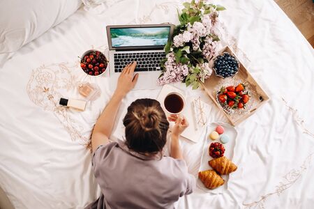 a girl sits in bed in the evening, with a smartphone in her hand and eats strawberries, a girl in...