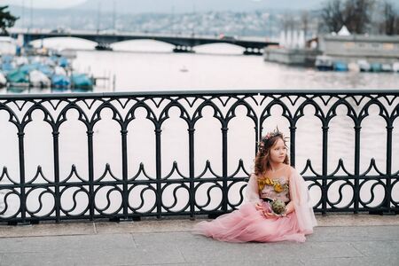 a little girl in a pink Princess dress with a bouquet in her hands walks through the old city of...