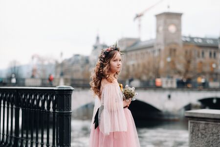 a little girl in a pink Princess dress with a bouquet in her hands walks through the old city of Zurich.Portrait of a girl in a pink dress on a city street in Switzerland.の写真素材