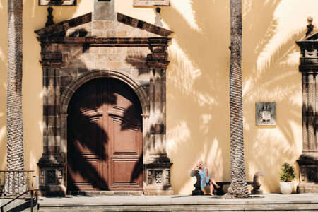 A girl in a blue dress sits on a bench in the old town of Garachico on the island of Tenerife on a Sunny day.A tourist walks in the old town on the island of Tenerife Canary Islands.Spain.の写真素材