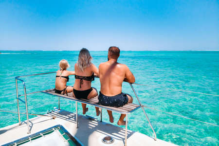 A young beautiful family with a child looks sitting on a yacht at the coral reef of the island of...