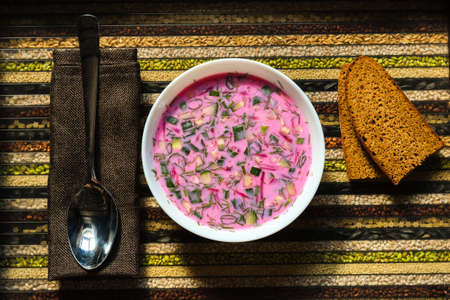 Cold beetroot soup on a spoon in your hand and bread on a decorative tray.Soup kholodnik red on an...