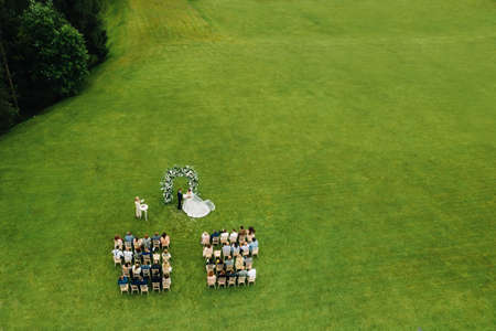 Top view of the Wedding ceremony in a green field with guests sitting on chairs. Wedding venue on the green lawnの写真素材
