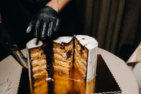 Amazing Cakes. A black-gloved chef is slicing a chocolate wedding cake. The wedding Cake is delicious inside on a black background.Large cake in white chocolateの写真素材
