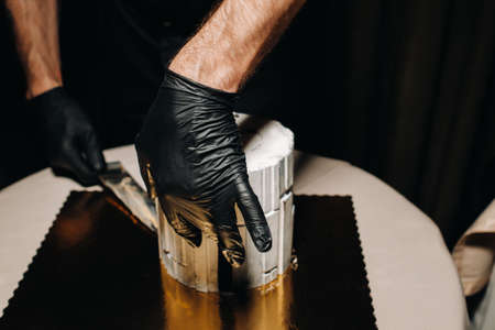 Amazing Cakes. A black-gloved chef is slicing a chocolate wedding cake. The wedding Cake is delicious inside on a black background.Large cake in white chocolateの写真素材