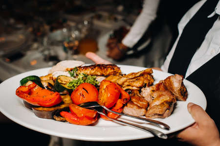 In the evening, the restaurant serves a hot dish of barbecue with vegetables.fried meat with tomatoes and other vegetables on a plate in a restaurantの写真素材
