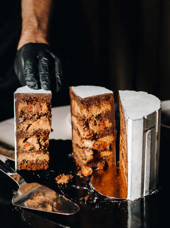Amazing Cakes. A black-gloved chef is slicing a chocolate wedding cake. The wedding Cake is delicious inside on a black background.Large cake in white chocolateの写真素材